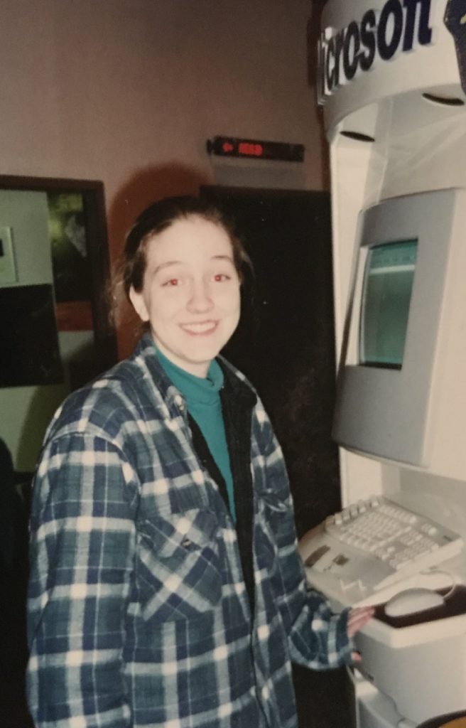 An image of  tiny babyRachel as a teenager in the '90s smiling awe-struck at a display of new technology.